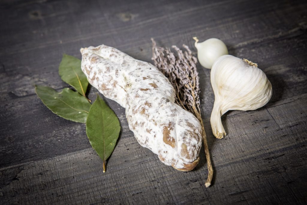 Saucisson présenté avec des feuilles de laurier, du thym et de l'ail