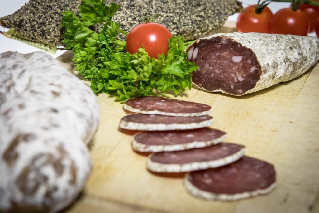 Saucisson au Beaufort présenté tranché sur une planche en bois, entourée de persil et tomates cerises.